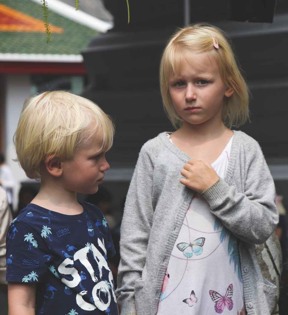 boy wearing blue and white stay cool print crew neck t shirt next to girl wearing white and teal butterfly printed scoop neck shirt and gray open long sleeved cardigan