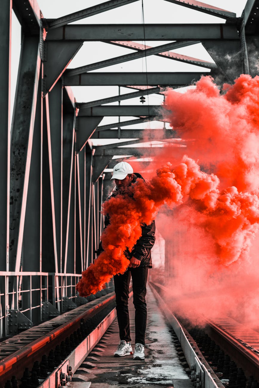 man in black jacket holding red smoke on metal bridge