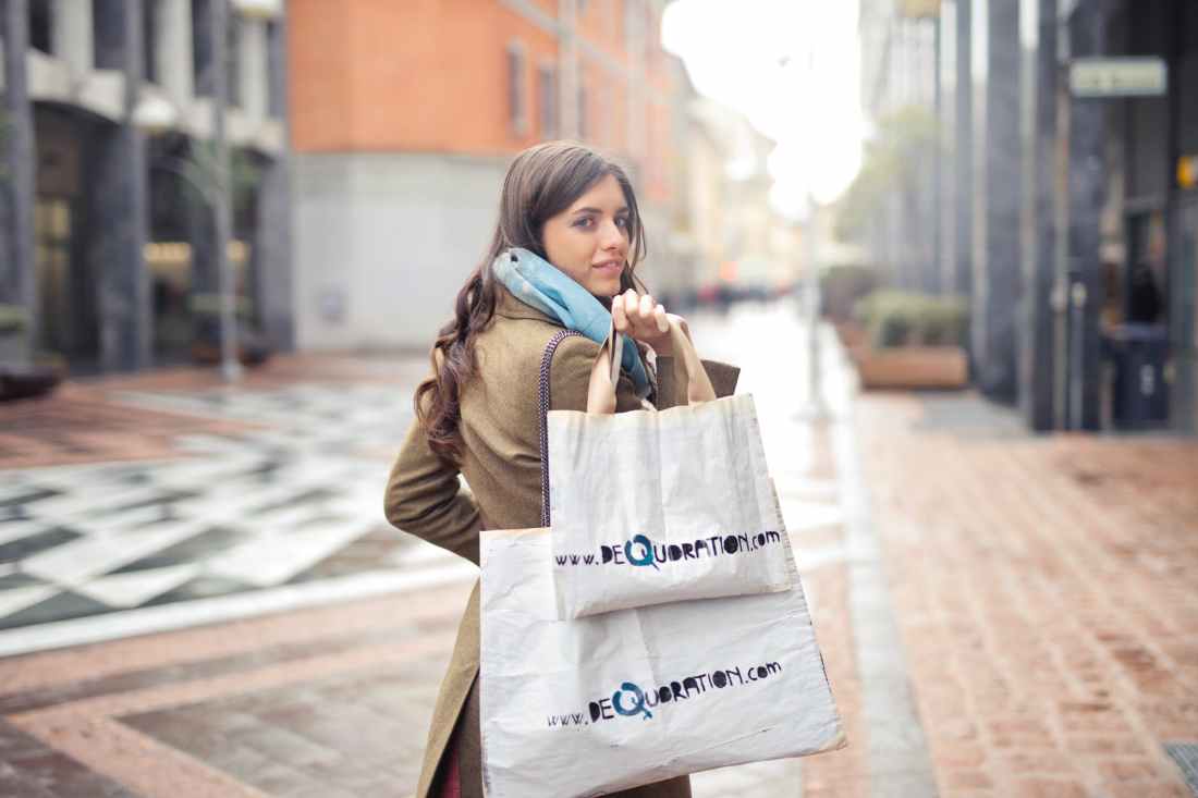 woman in brown coat carrying two white tote bags