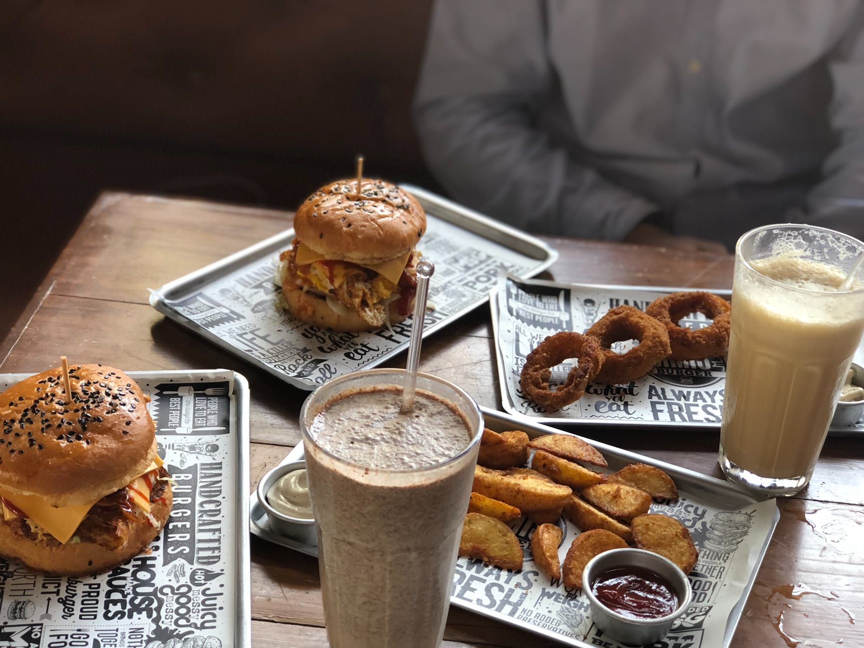 two milk shakes burgers fried onion rings and wedge potatoes on the table