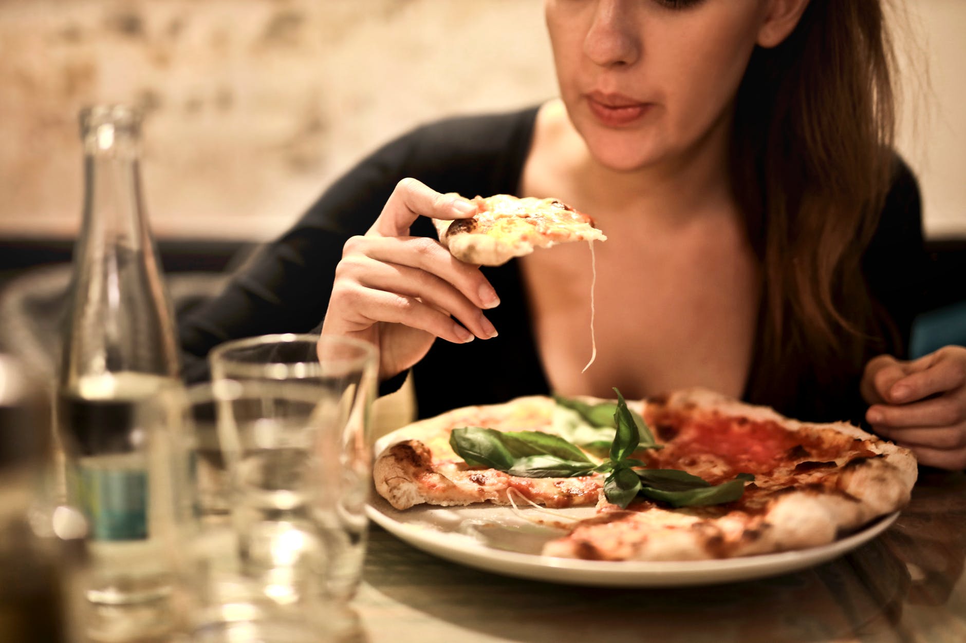 woman holds sliced pizza seats by table with glass