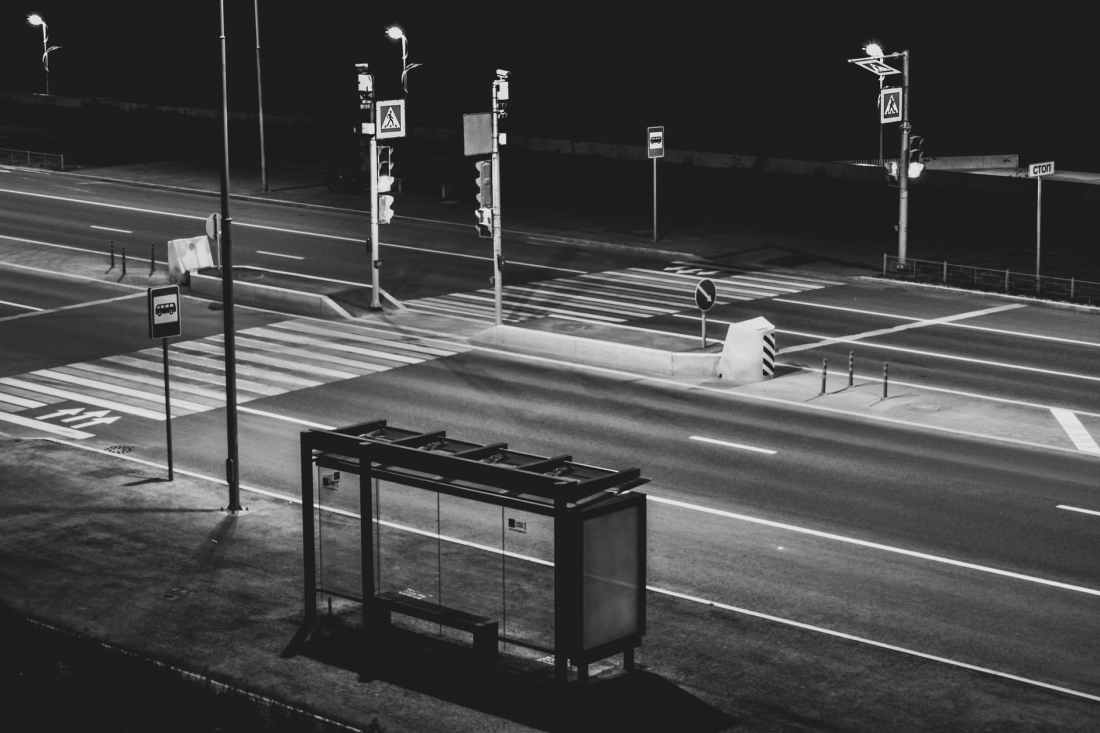 grayscale photography of waiting shed near open road at night