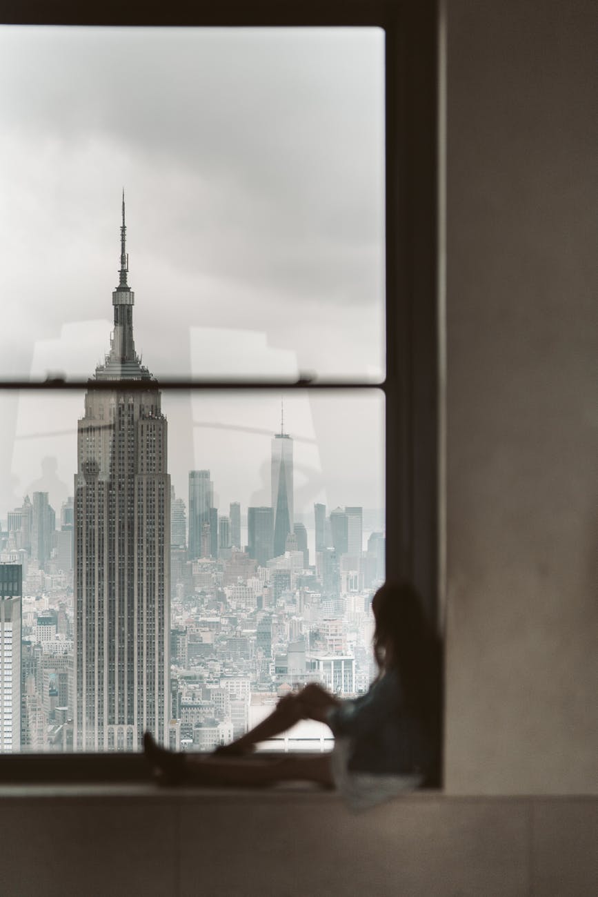 woman sitting at window sill looking out the window at new york city